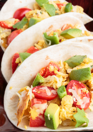 Tacos filled with migas, a Tex-Mex dish of eggs scrambled with red bell pepper, onions, jalapenos, cheese, topped with avocado, cilantro, cherry tomatoesの写真素材