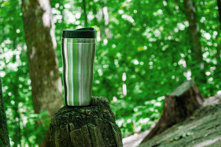 Thermo mug standing on a log in the forest against the background of green trees