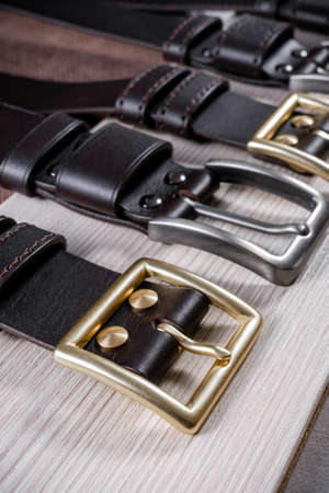 Leather belts with gray and gold buckles lie on a geometric wood background