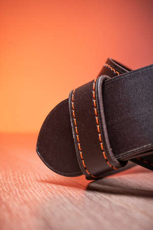 The leather brown belt rests on a wooden board on an orange background close-up