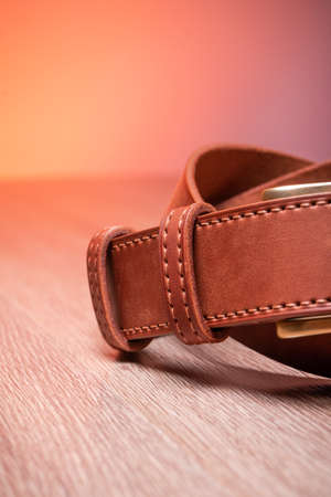Leather brown belt twisted in a sign of infinity on a wooden orange background. High quality photoの写真素材