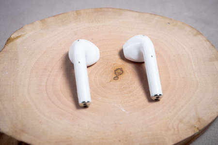 White wireless headphones on a cut of a tree with a gray background