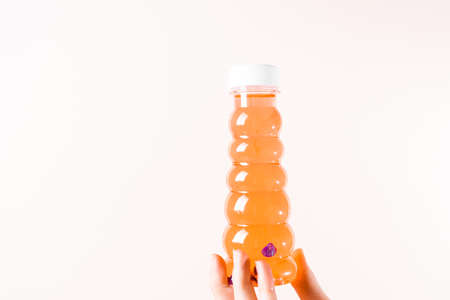 A jar of orange slime is held by the girls fingers on a light beige backgroundの写真素材