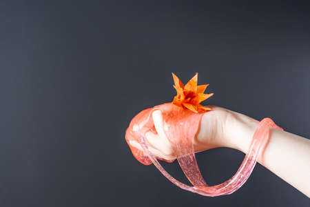 The flower of paper rests on the hand with which the slime flows on a gray background