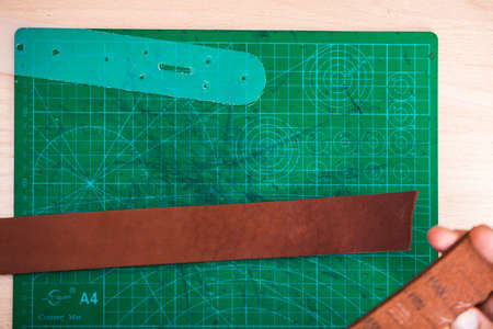 The leather blank for the belt rests on a green stand next to the stencil
