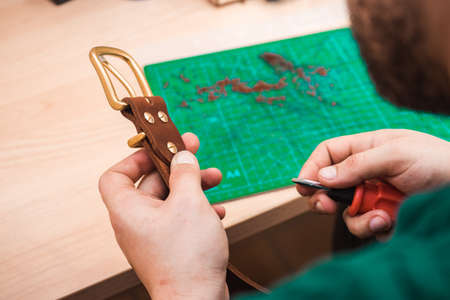 Hands attach a gold buckle to the blank of the leather belt