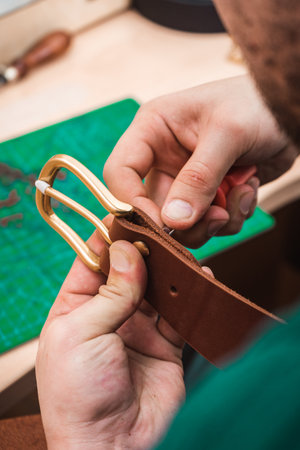 The leather master fastens the gold buckle to the brown belt