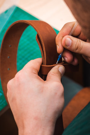 Hands sew a brown belt with threads and a needleの写真素材