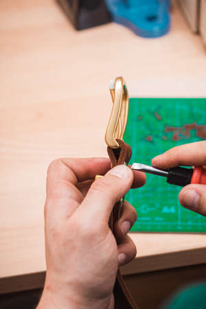 The leather master fastens the gold buckle to the brown belt