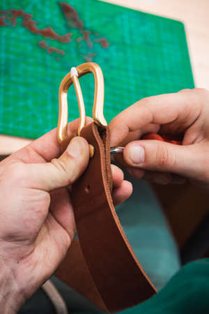 Hands attach a gold buckle to the blank of the leather belt