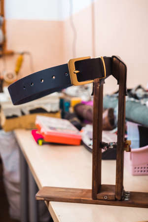 Blue leather belt with gold buckle against the background of the leather masters workplace