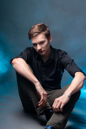 Portrait of a young man against the background of smoke illuminated by blue lightの写真素材
