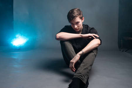Sad young man in black shirt sits on a gray background with smoke blueの写真素材