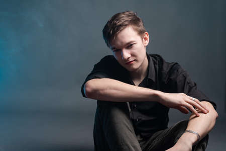 Tense man in black shirt on grey background, illuminated by blue lampsの写真素材