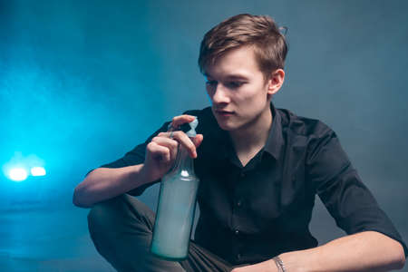 A man looks at a bottle of alcohol amid blue smoke