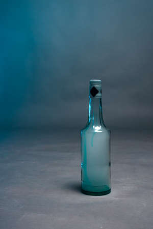 A bottle of alcohol filled with smoke stands on a gray background with blue glareの写真素材