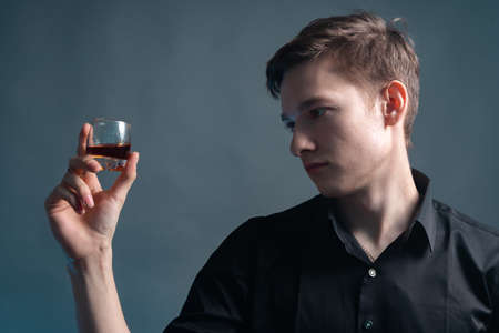 A young man holds a glass of rum on a gray backgroundの写真素材