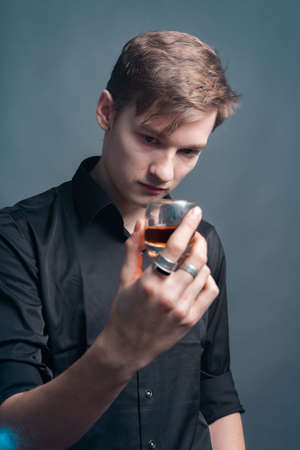 The guy holds a glass of whiskey on a gray backgroundの写真素材