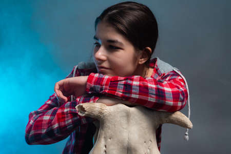 Portrait of a girl who rests on a bulls skull, on a gray background with blue smokeの写真素材