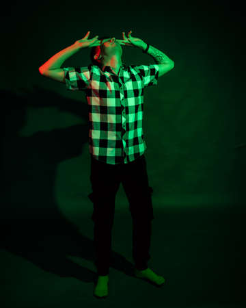 A young man in a plaid shirt in a studio with red and green light on a black backgroundの写真素材
