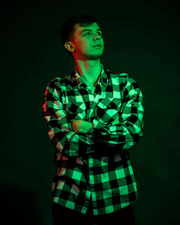 A young man in a plaid shirt in a studio with red and green light on a black background