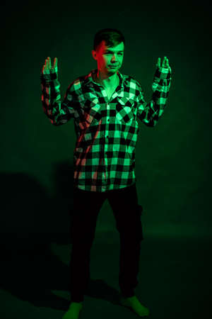 A young man in a plaid shirt in a studio with red and green light on a black backgroundの写真素材