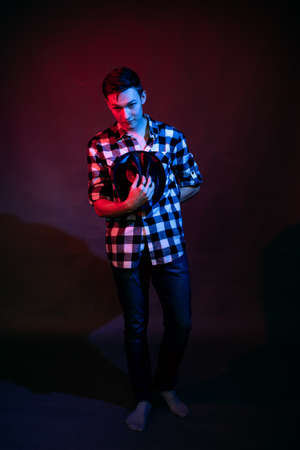 A guy in a plaid shirt with red and blue lighting in the studio on a black backgroundの写真素材