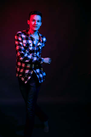 A guy in a plaid shirt with red and blue lighting in the studio on a black backgroundの写真素材
