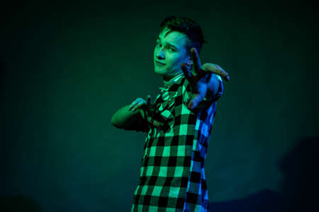 A young man in a studio on a dark background with a multicolored lightの写真素材