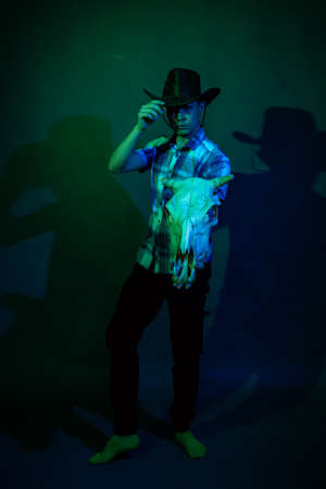A guy in a cowboy hat and a plaid shirt in a studio with blue and green lightの写真素材