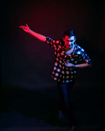 A young man in a studio on a dark background with a multicolored lightの写真素材