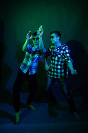 Two young men in plaid shirts dance in the studio with multicolored lightの写真素材
