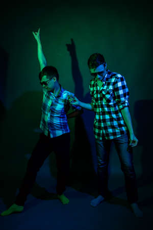 Two young men in plaid shirts dance in the studio with multicolored lightの写真素材