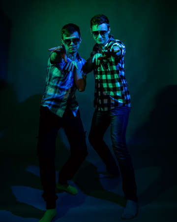 Two young men in plaid shirts dance in the studio with multicolored lightの写真素材