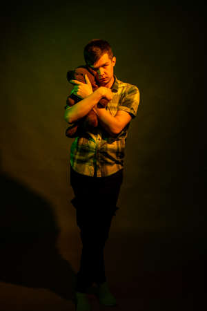 The guy plays with a teddy bear, illuminated by yellow and green lightの写真素材