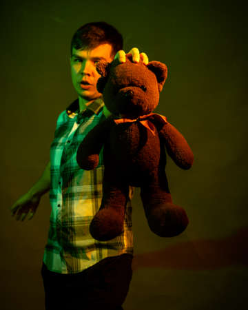 The guy plays with a teddy bear, illuminated by yellow and green lightの写真素材