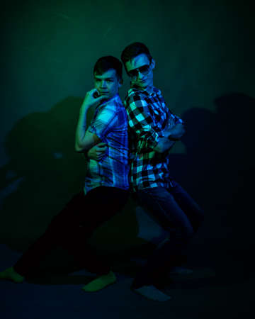 Two young men in plaid shirts dance in the studio with multicolored lightの写真素材