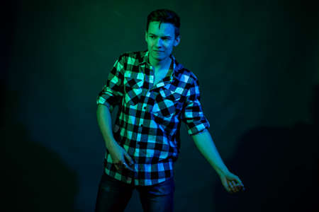 A young man dances in the studio with blue and green lightの写真素材