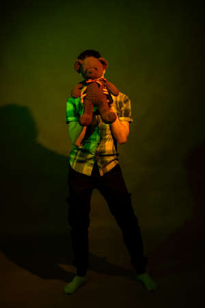 The guy plays with a teddy bear, illuminated by yellow and green lightの写真素材
