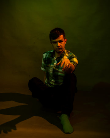 A young man sits on the floor. illuminated by multicolored lightの写真素材