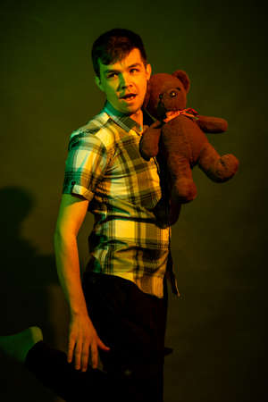 The guy plays with a teddy bear, illuminated by yellow and green lightの写真素材