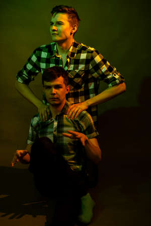 Two guys sitting on the floor in the studio. illuminated by yellow and green lightの写真素材
