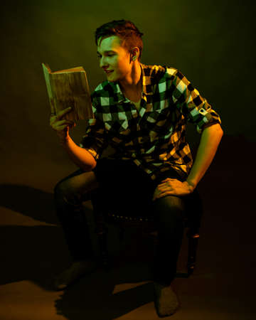 A guy in a plaid shirt reads a book lit by multicolored lightの写真素材