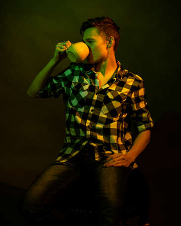 A young man sits on a dark background illuminated by green and yellow light as in a movie
