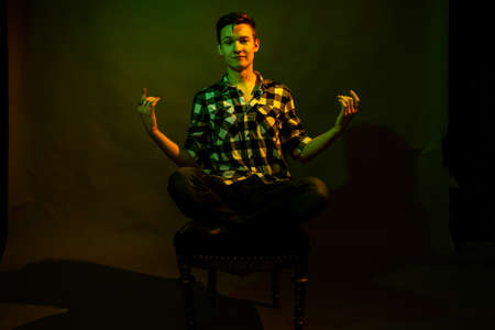 A young man sits on a dark background illuminated by green and yellow light as in a movieの写真素材