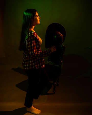 A girl in a plaid shirt with a cowboy hat illuminated by multicolored lightの写真素材
