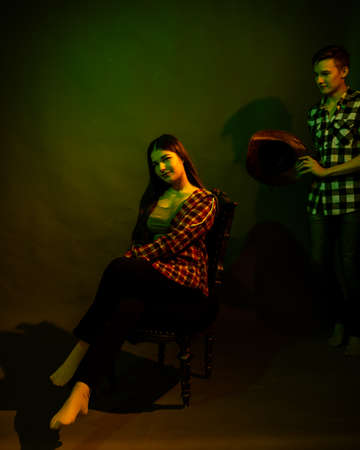 The girl sits on a black chair illuminated by multicolored lightの写真素材