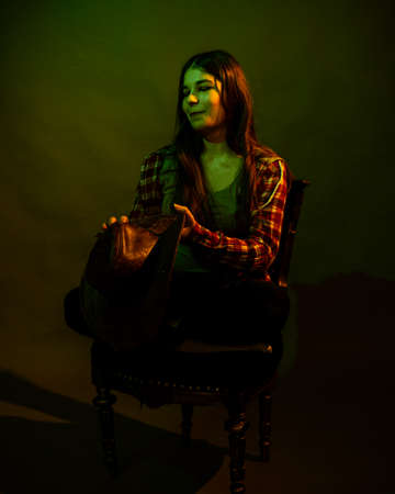 The girl sits on a black chair illuminated by multicolored lightの写真素材