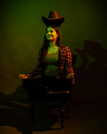 The girl sits on a black chair illuminated by multicolored lightの写真素材