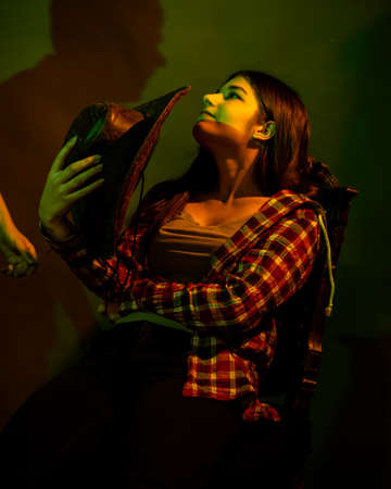 The girl sits on a black chair illuminated by multicolored light
